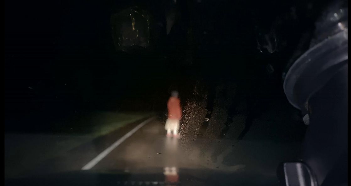 Una mujer se para en medio de una carretera en la noche iluminada por los faros de un automóvil en Dashcam.