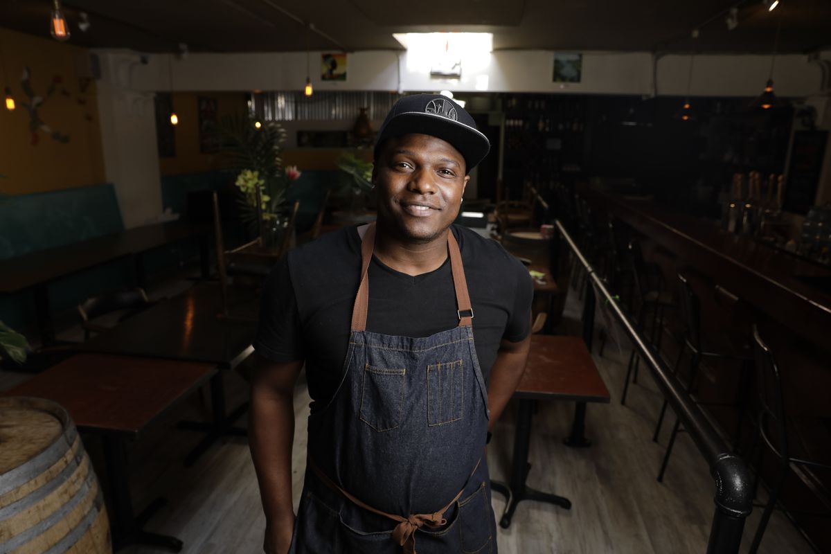 A Black man in a chef’s apron standing in an empty restaurant