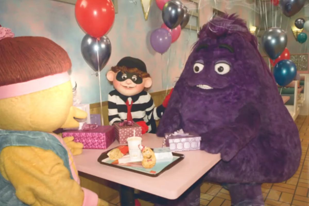 An old photo of Grimace, the Hamburgler, and a Birdie and Early Bird sitting around a table, eating McDonald’s.