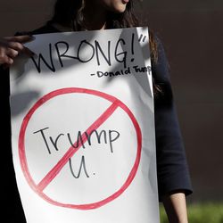 Senya Merchant holds a sign against President-elect Donald Trump's now-defunct Trump University Friday, Nov. 18, 2016, in San Diego. Trump agreed Friday to pay $25 million to settle several lawsuits alleging that his former school for real estate investors defrauded students who paid up to $35,000 to enroll in Trump University programs.