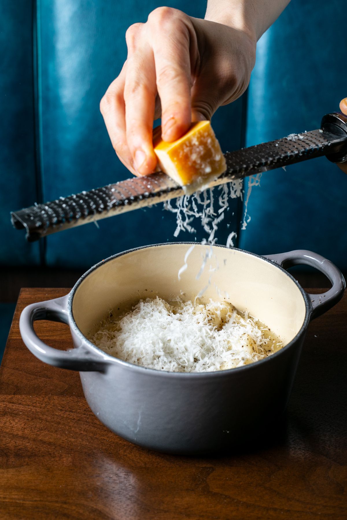 A staffer shaves Parmesan over a  grey glazed pot holding cacio e pepe rice cakes