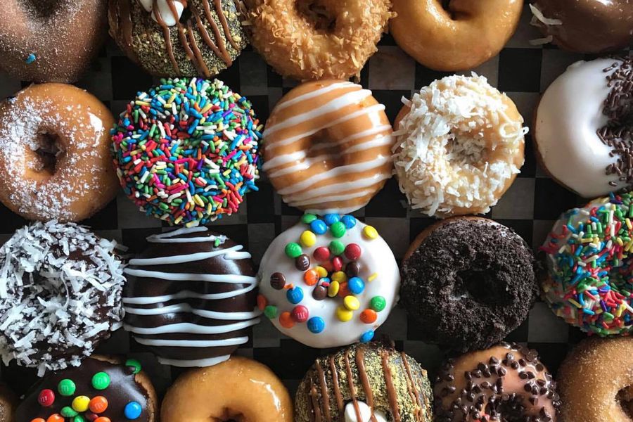 A large assortment of doughnuts including doughnuts topped with sprinkles, chocolate glaze, and coconut.