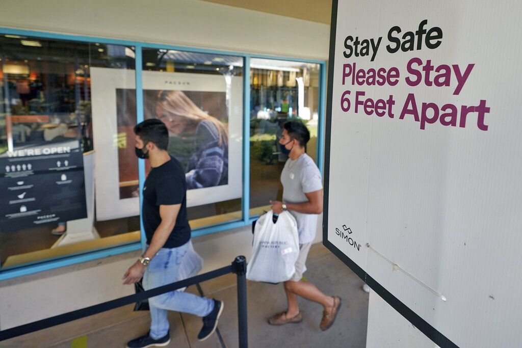 Shoppers wear protective face masks as they walk past a social distancing sign at the Ellenton Premium Outlet stores Friday, Nov. 27, 2020, in Ellenton, Florida.