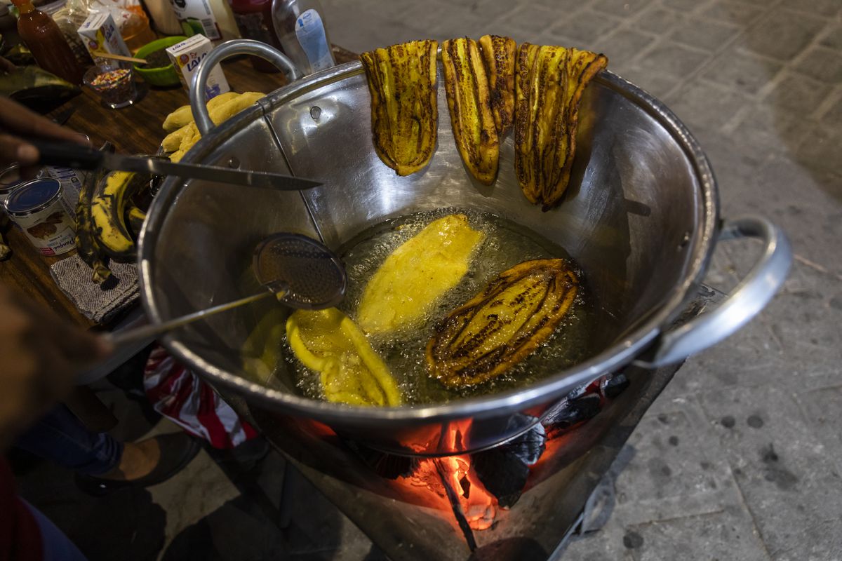 Sliced plantains frying in oil in a metal pot.