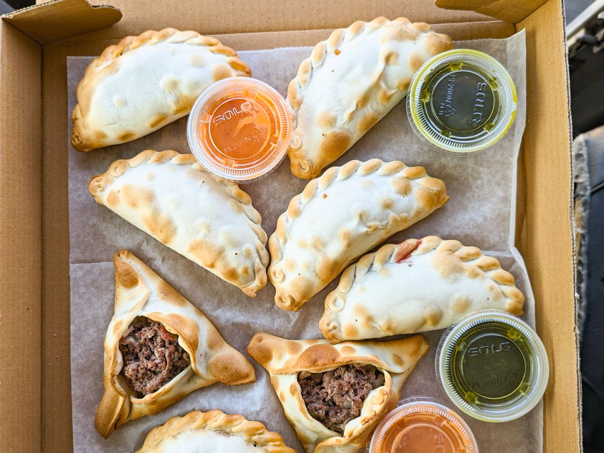 Argentinian empanadas in a pizza box with sides of chimichurri and salsa criolla