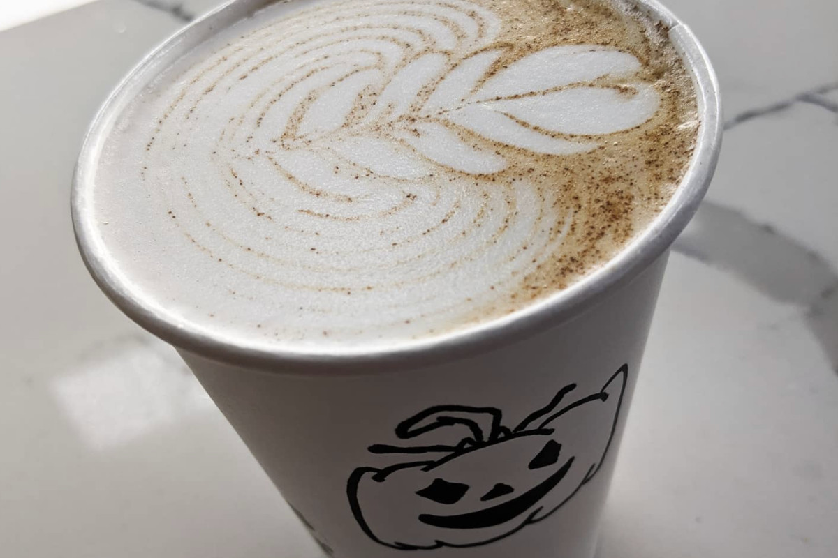 A paper cup with a drawing of a pumpkin on it, filled with a latte that has a floral design