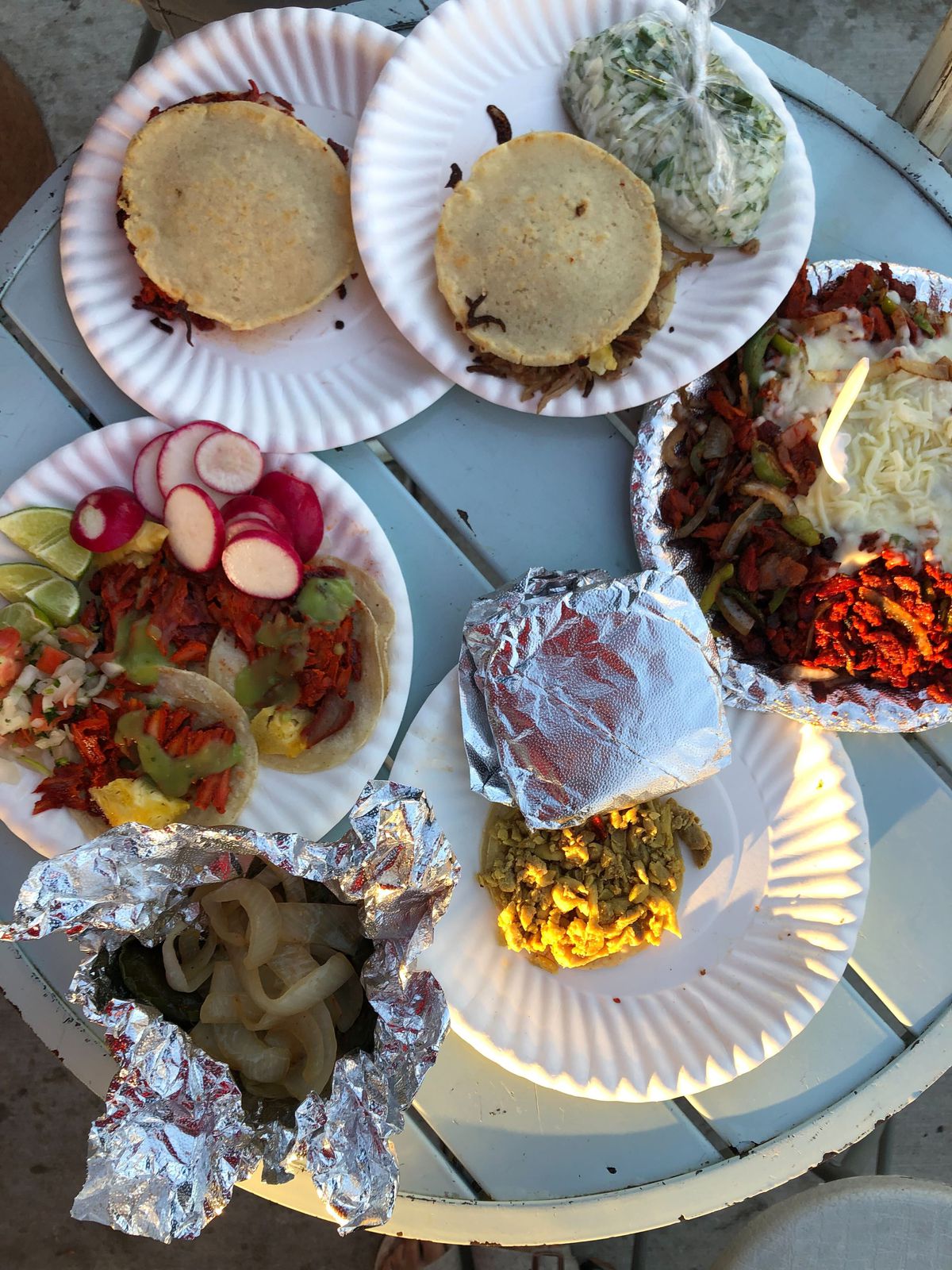 A wooden table laden with tacos on paper plates.