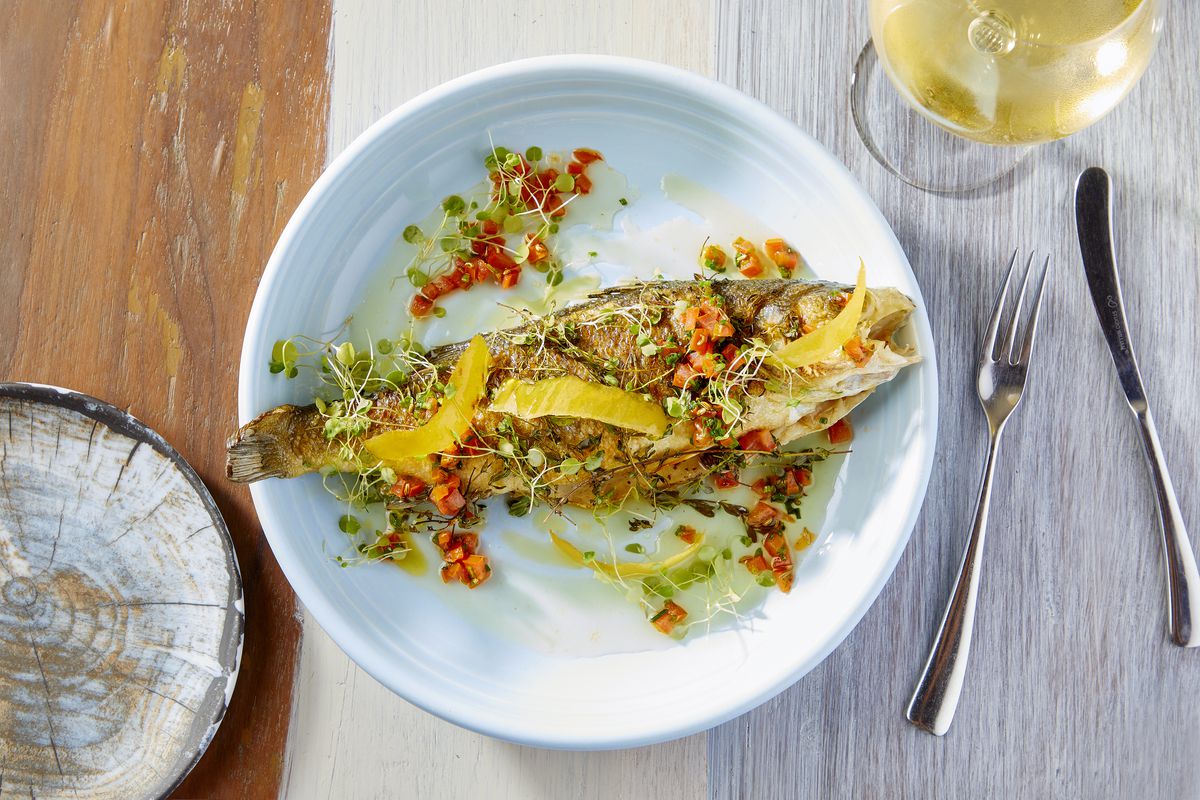 A large whole fish on the bone with colorful Mediterranean accoutrements on a white plate