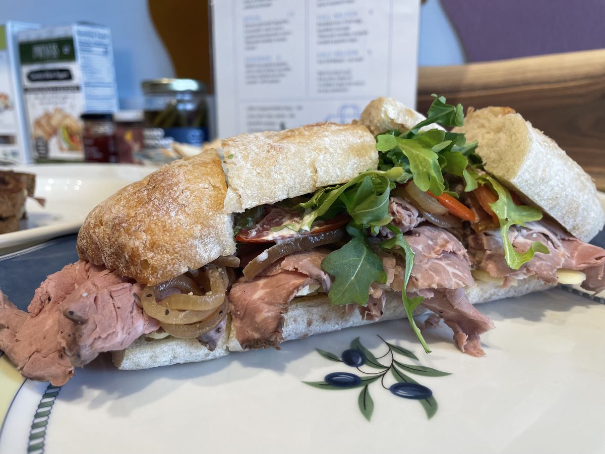 A roast beef sandwich with onions, peppers, and arugula on a white plate.