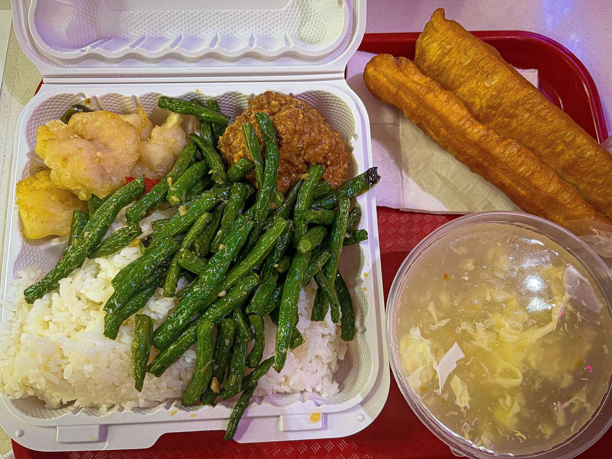 A lunch spread includes egg drop soup, fried dough, and a tray of rice topped with green beans.