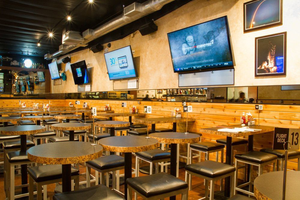 Square tables and black stool seating inside a sports bar.