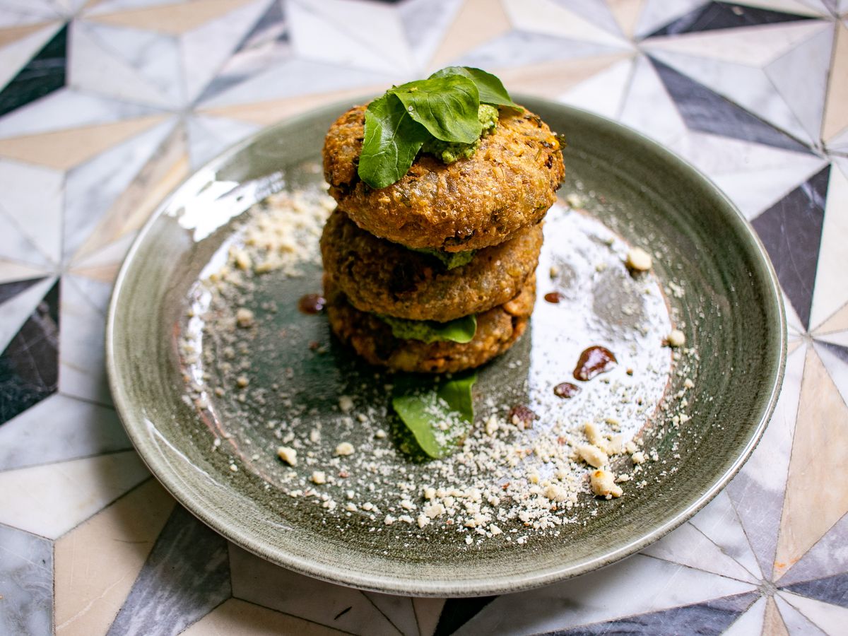 A light green round plate with three brown fritters stacked on top of each other with a spoonful of green chutney placed between each fritter.