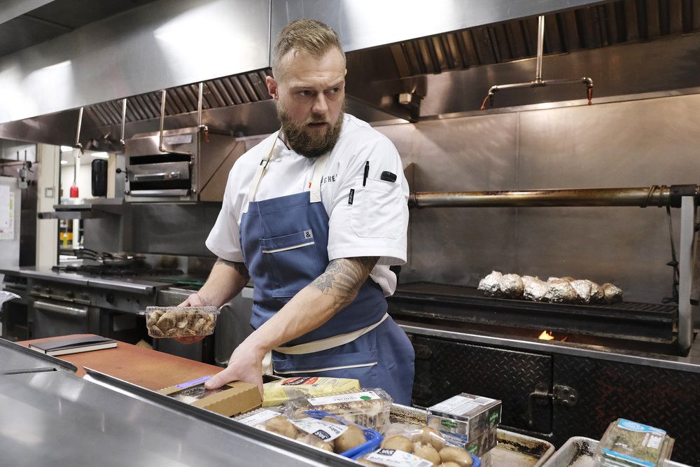 Chef Luke Kolpin, in a blue apron, organizes ingredients during a challenge.