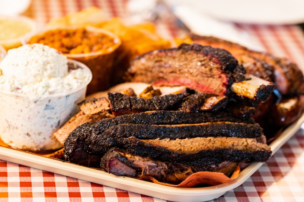 A tray holds brisket, ribs, potato salad, pinto beans, and more barbecue.