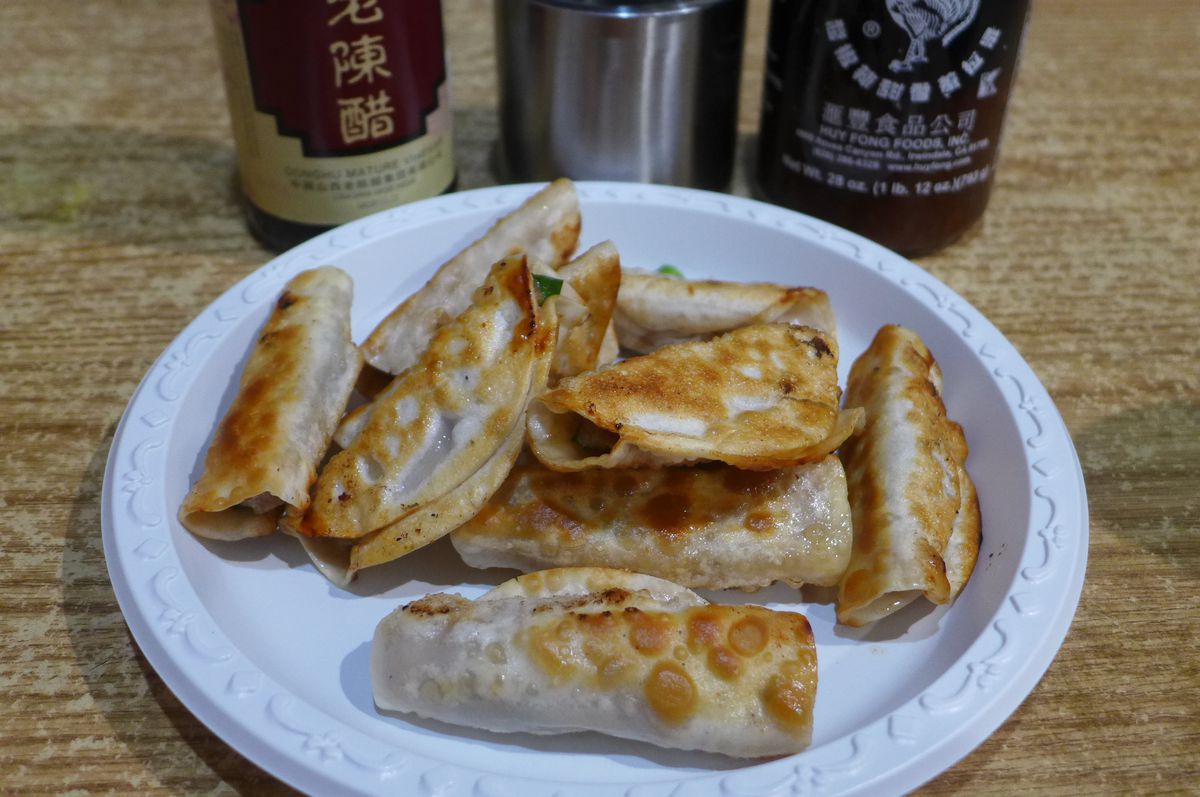 A white plate with browned dumplings on it and three bottles of sauce behind.