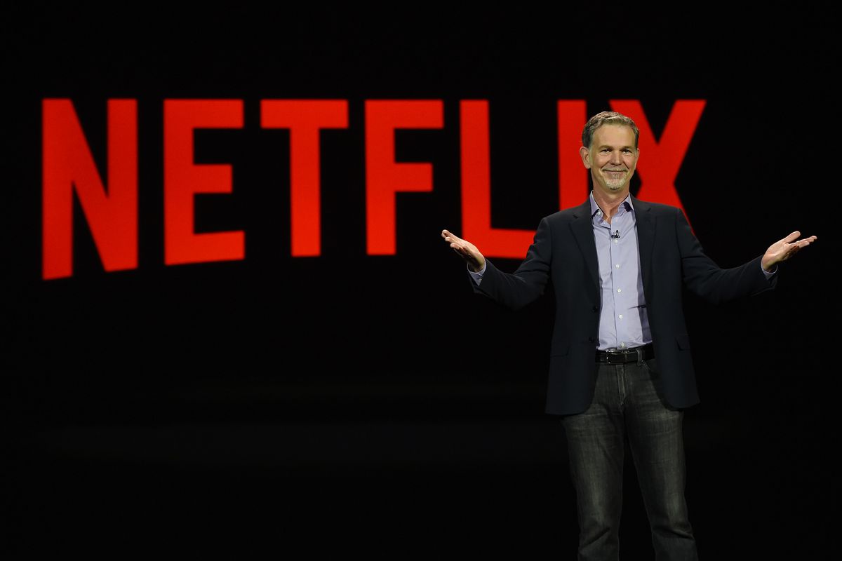 Netflix CEO Reed Hastings&nbsp;stands in front of a sign that reads “Netflix.”