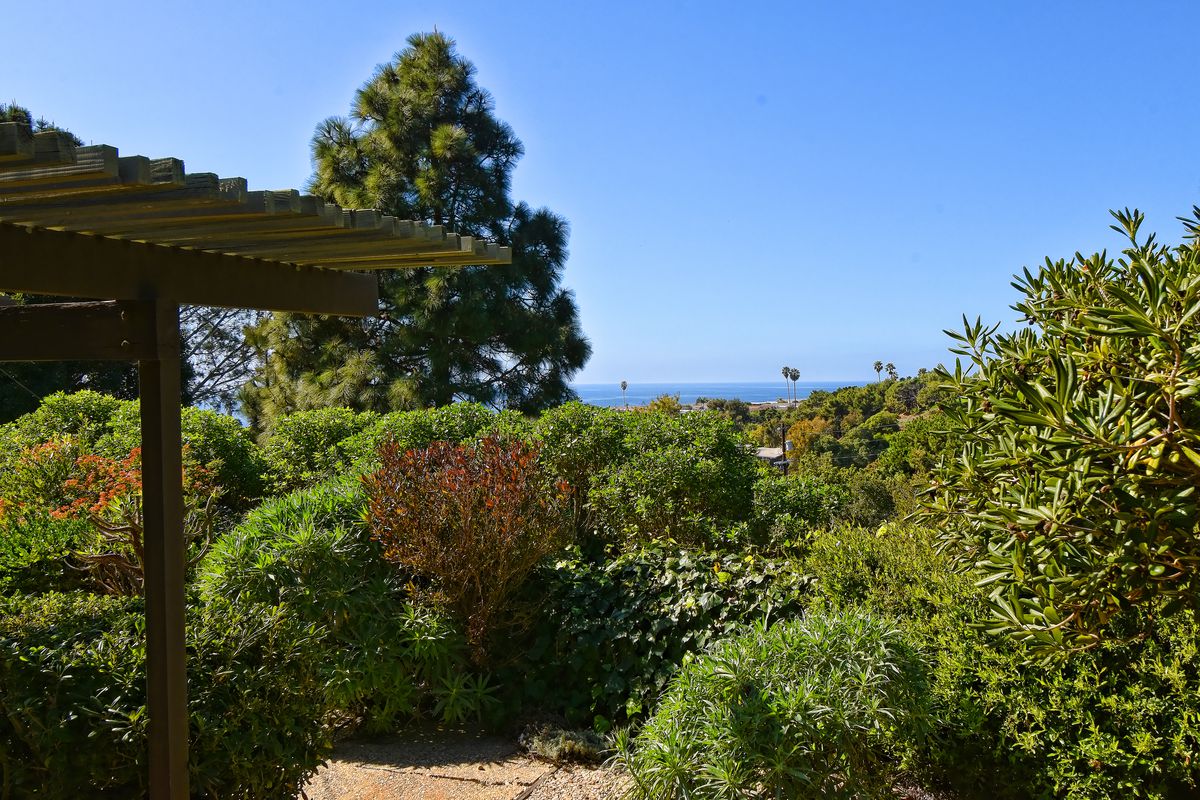 A pergola surrounded by bushes and trees, with the ocean visible in the distance