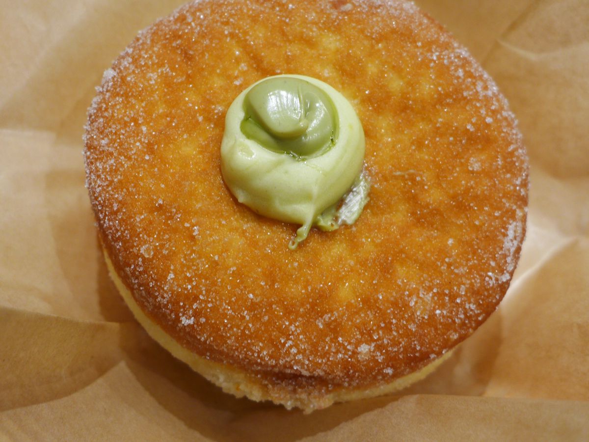A round doughnut with a dab of green filling coming out in the middle.