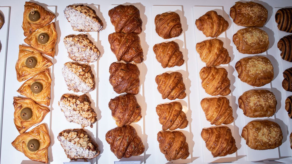 An overhead shot of a spread of croissants and other pastries lined up by type on white butcher paper.