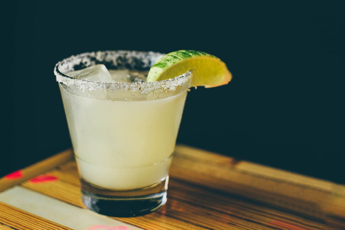 A margarita on a wooden table with heavily salted rim and a lime.
