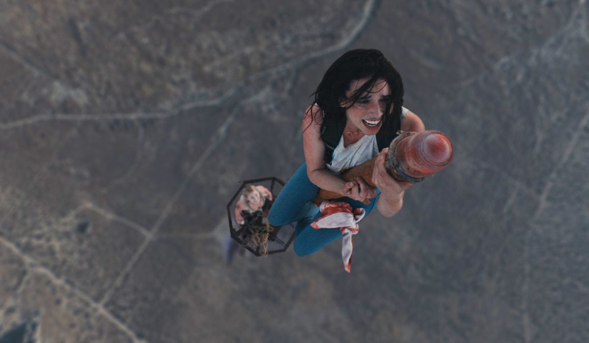 A woman looking visibly distressed as she climbs to the top of a radio tower in a desert.