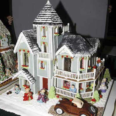 Gingerbread house in the shape of Queen Anne style home, with marzipan people placed around it. 