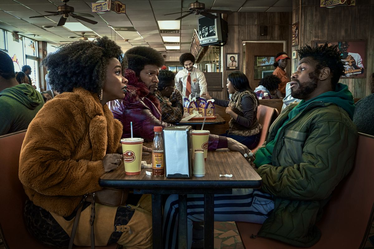 (L to R) Teyonah Parris as Yo-Yo, Jamie Foxx (Producer) as Slick Charles and John Boyega as Fontaine sitting across from one another at a fast food restaurant in They Cloned Tyrone.