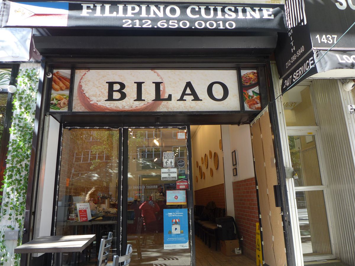 A plainish storefront that says Filipino Cuisine, with a table out front.