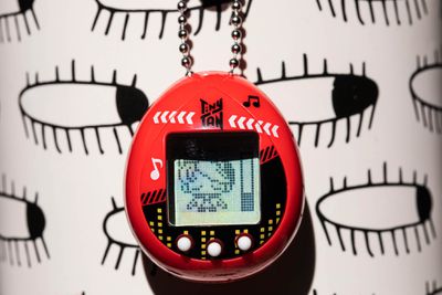 A user holds the TinyTan Tamagotchi. The screen displays a character sleeping with a stamina bar a quarter full beside it.