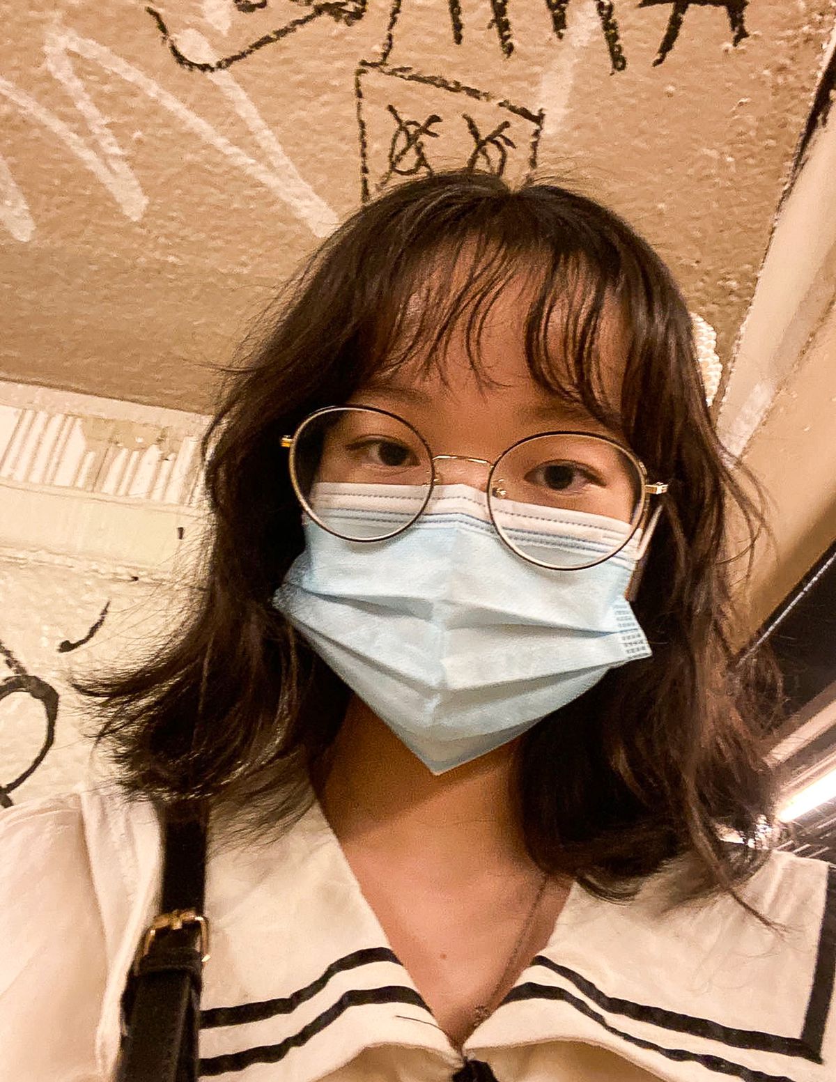 A teenage girl poses for a selfie, wearing glasses and a blue surgical mask.