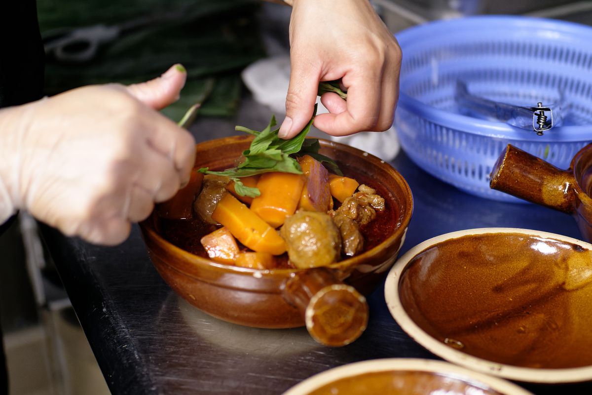 A person places green leaves atop a bowl of stew.