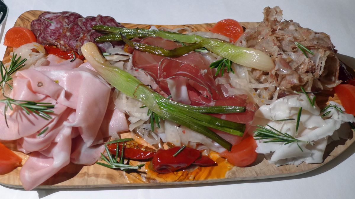 A cutting board draped with different kinds of cured meat in pink and white.