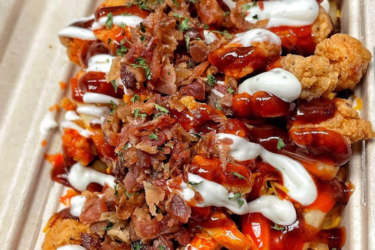 A platter of fries with barbecue sauce, ranch dressing, fried chicken, and bacon