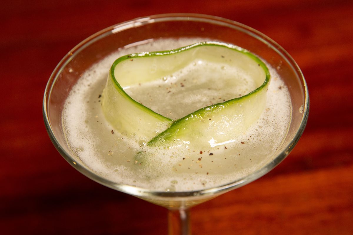 A cocktail in a martini glass with a big slice of cucumber