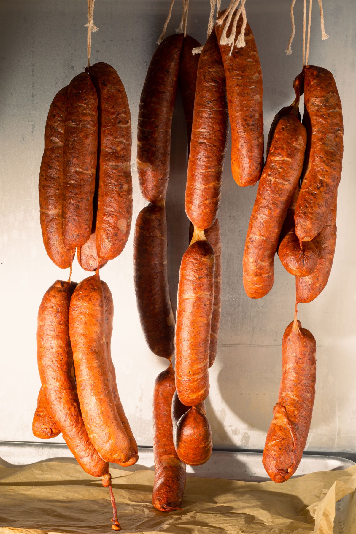 Strings of sausages hang over a piece of parchment paper.