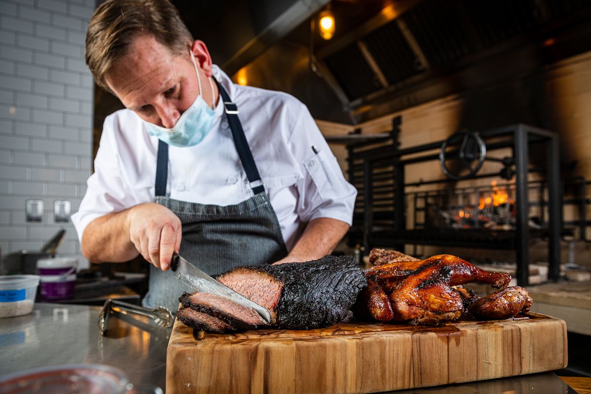 Ruthie’s All Day chef Matt Hill wears a disposable face mask while he slices brisket