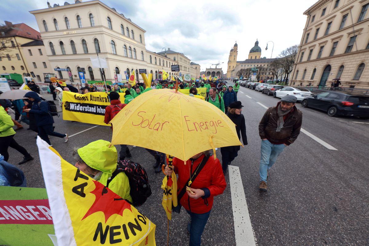 People with banners in German march through the street. One person holds an umbrella that reads “solar energie.”