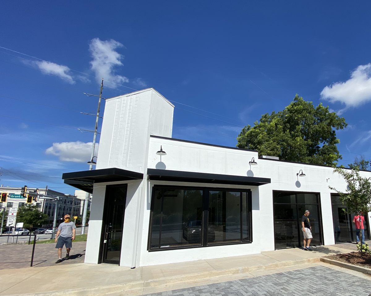 A side view of the crisp white painted building that will house Das BBQ in Grant Park, three men are walking around the side of the building