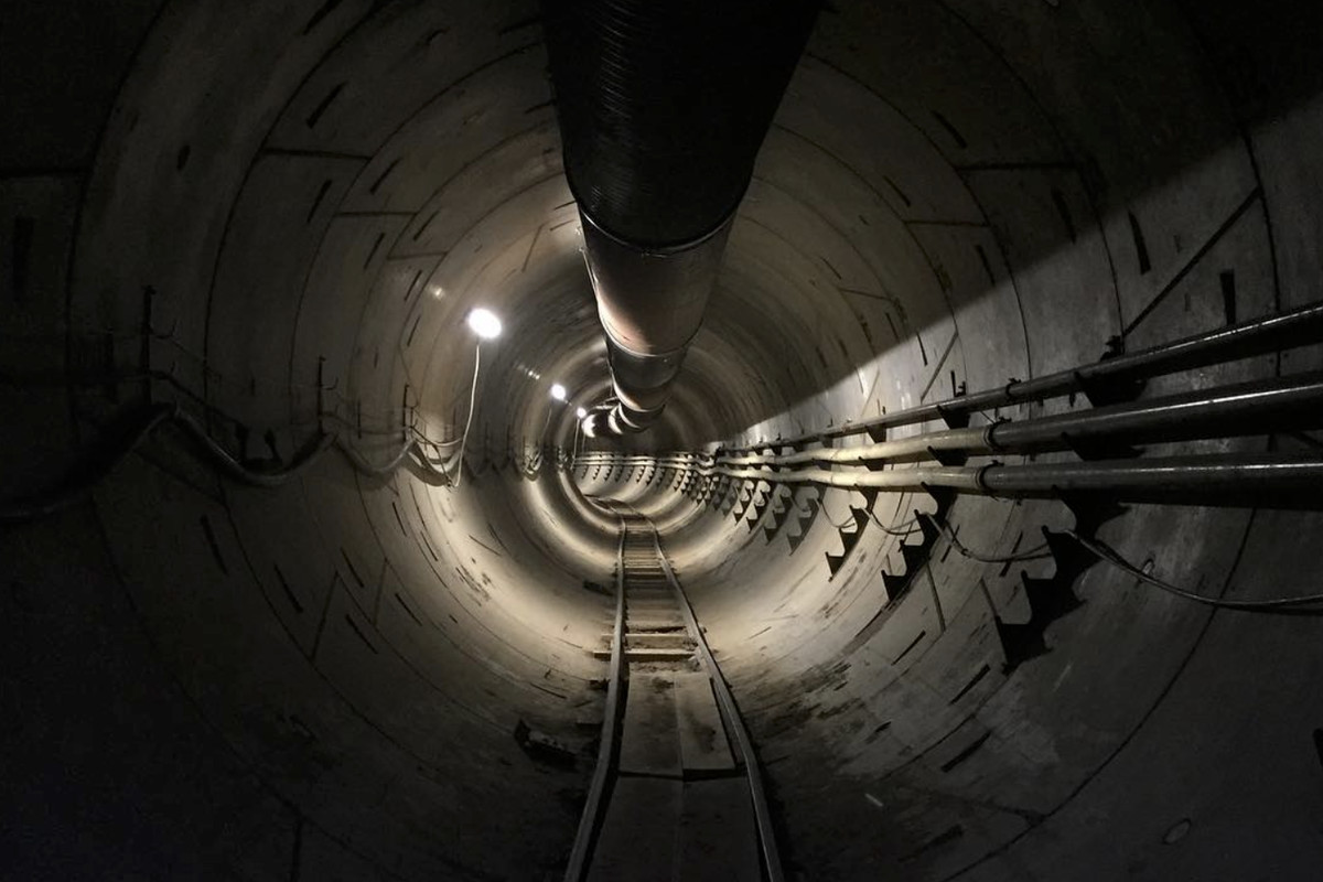 A concrete tunnel with pipes along one side and the ceiling, wires along the other side and tracks along the bottom