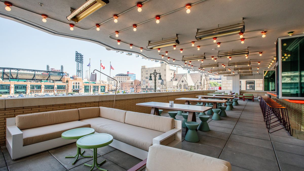 A patio with an indoor-outdoor bar and varied sofa and table seating looks out onto Woodward and Comerica Park