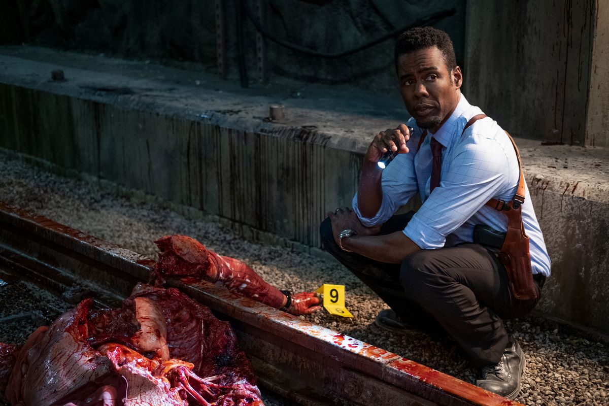 Chris Rock squats by a skinless, shredded human body on train tracks in Spiral: From the Book of Saw