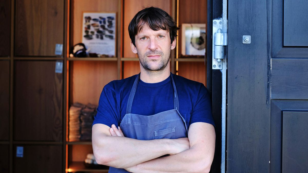 Rene Redzepi stands in a doorway, wearing an apron and crossing his arms.