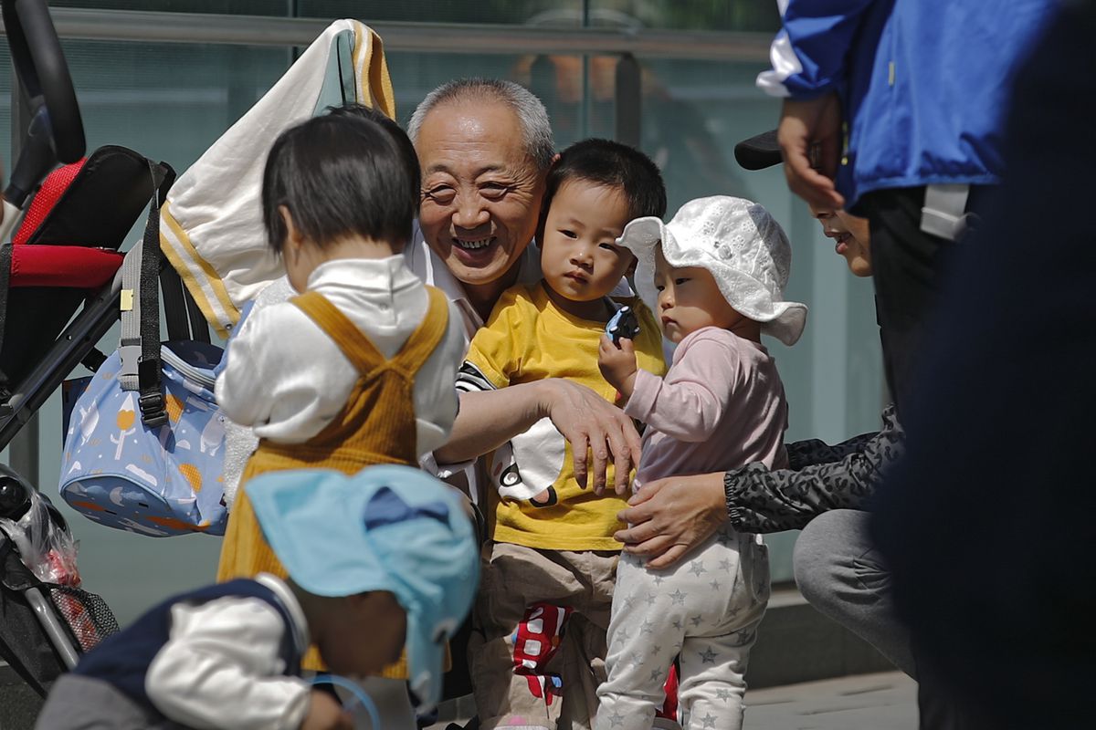 An elderly man plays with children near a commercial office building in Beijing on May 10, 2021. China’s ruling Communist Party will ease birth limits to allow all couples to have three children instead of two to cope with the rapid rise in the average age of its population, a state news agency said Monday, May 31.