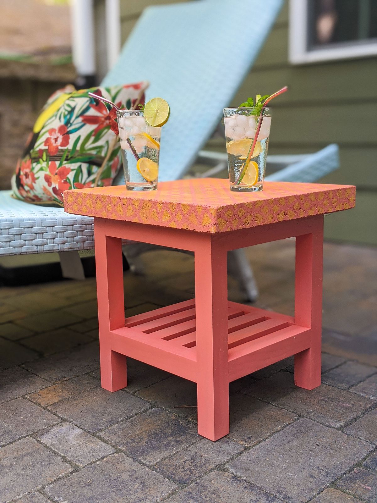 A coral colored side table with a patterned patio paver on top. 