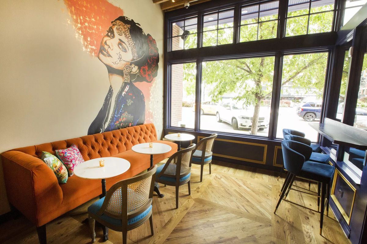 Rooh’s dining room features high top seating, an orange couch, and a painted mural called Christine by Jenny Vyas,