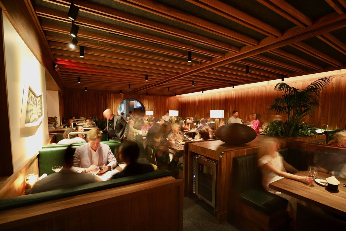 Balboa Surf Club’s dining room features various booths with emerald green seating and wooden beams.