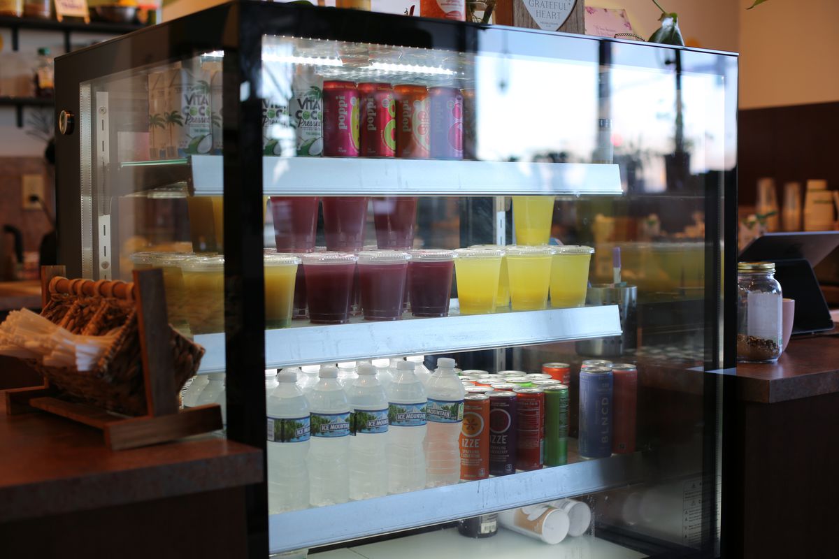 A glass case with shelves of fresh-pressed juices, waterbottles, and canned sodas and juices. 