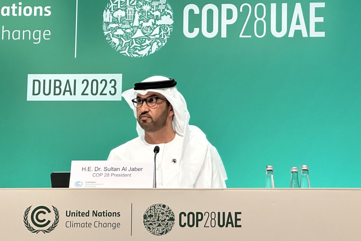 A man wearing a white robe and head scarf with a black headband, sitting at the COP28 speakers’ desk.