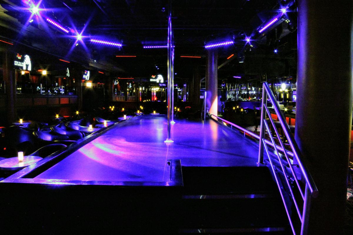 An empty strip club with a stage and pole surrounded by chairs.
