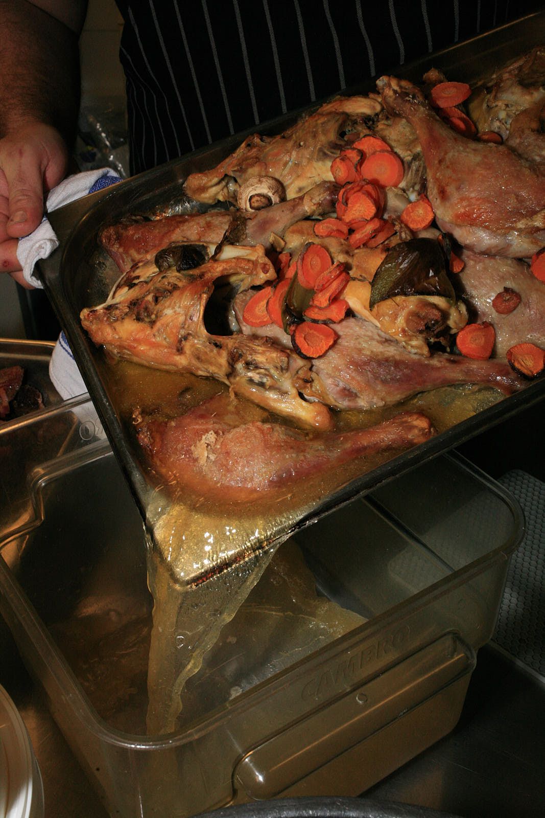 Duck fat is poured out of the metal gastro that housed the roasted duck legs and vegetables, into a clear stock jug.